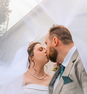 A newlywed couple sharing a tender kiss under the white veil.